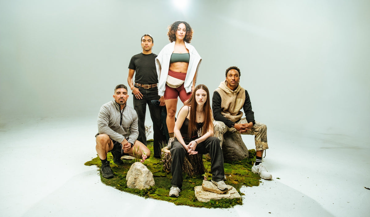 Five Vybrance Labs community members gathered on a moss-covered set, two women at the center, in a studio