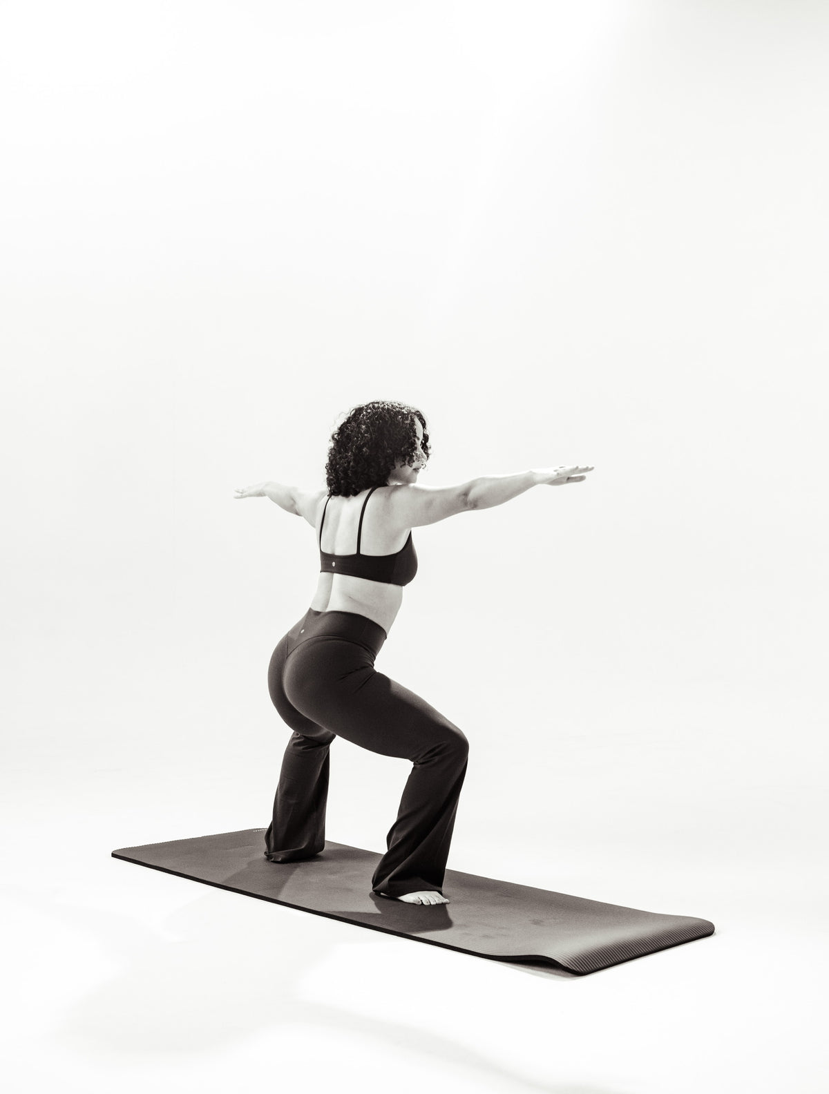 A woman holds a wide squat with both arms extended on an exercise mat, in black and white