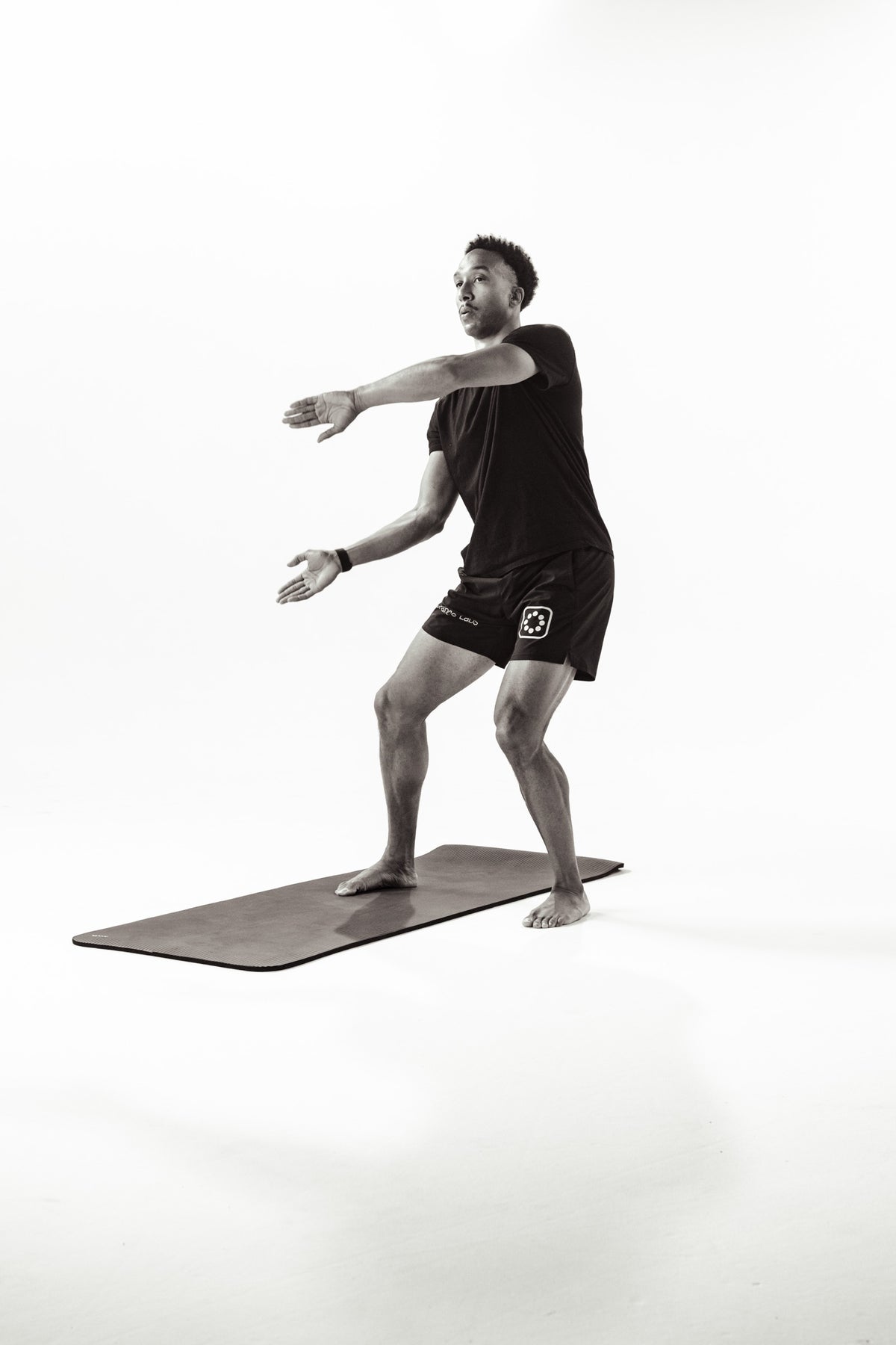 A man standing on a mat in a wide stance with both arms extended in front of him