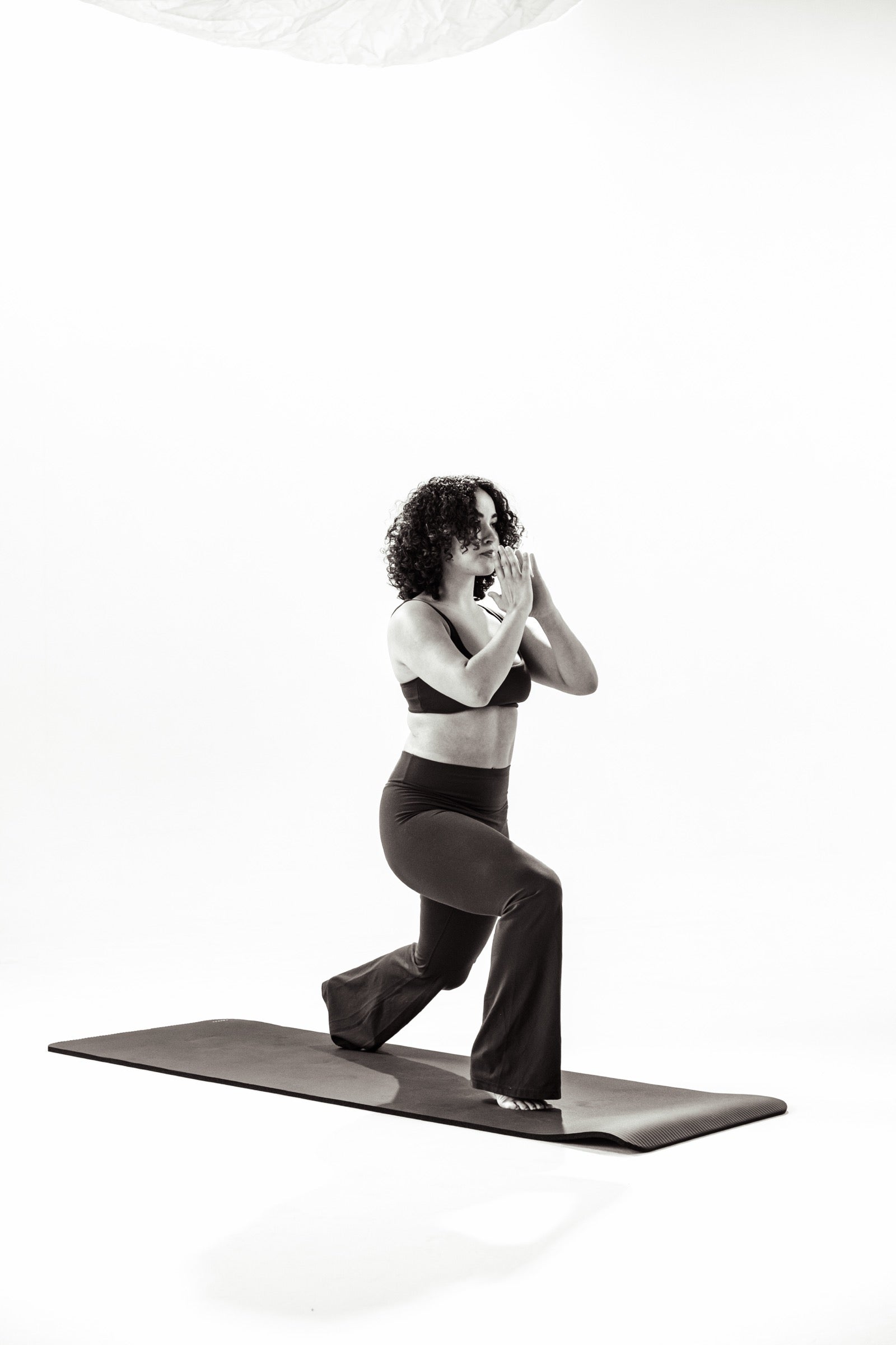 A woman holding a low kneeling lunge on a mat against a white studio backdrop