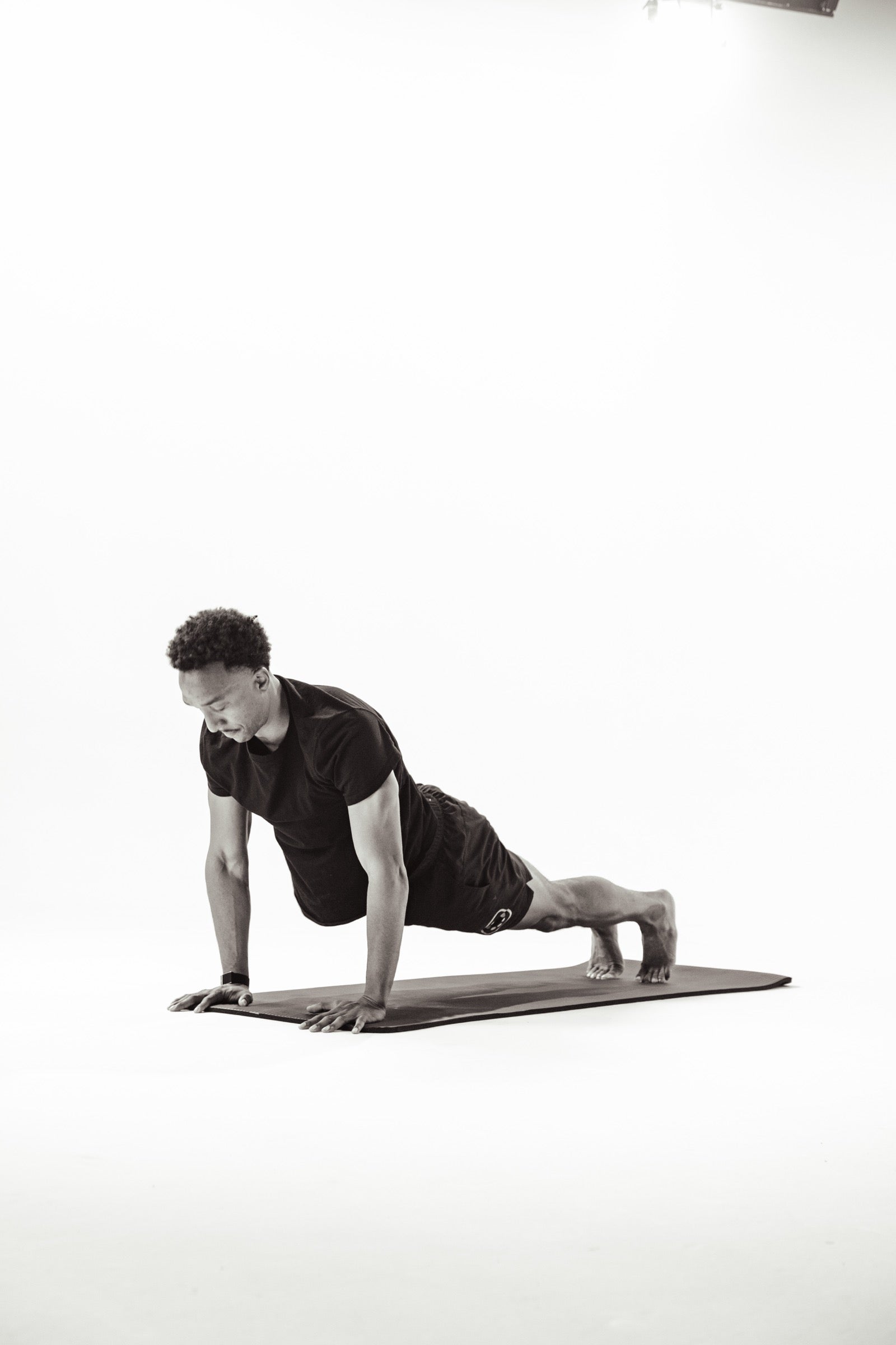 A person holding a high plank position on a mat against a white studio backdrop