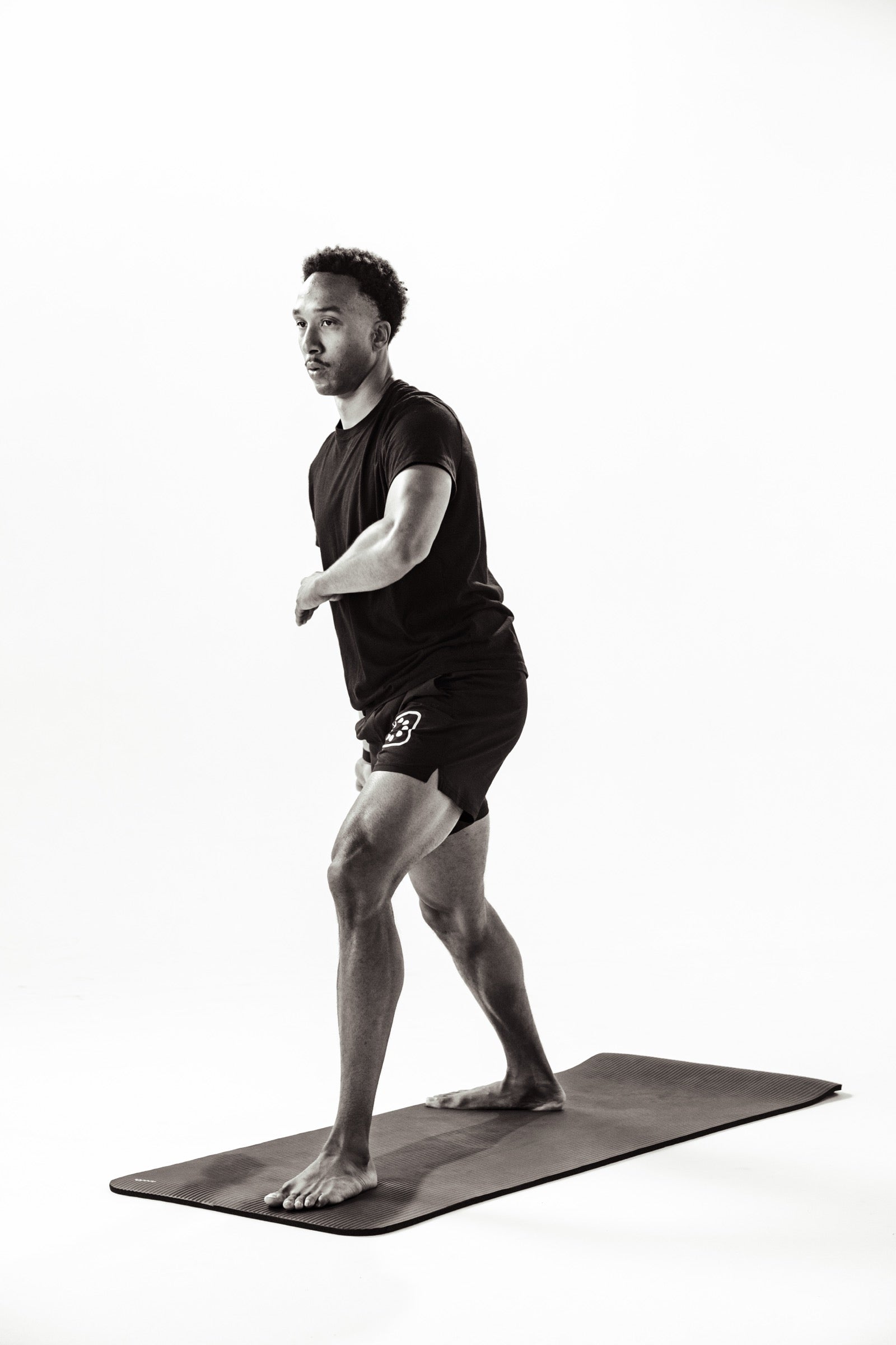 A man mid stride in a standing lunge on a mat against a white studio backdrop