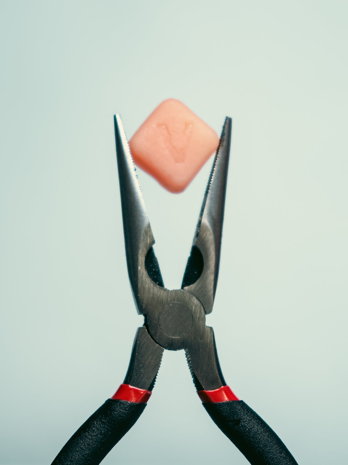 A pair of needle nose pliers holding a single Vybrance gummy against a pale background