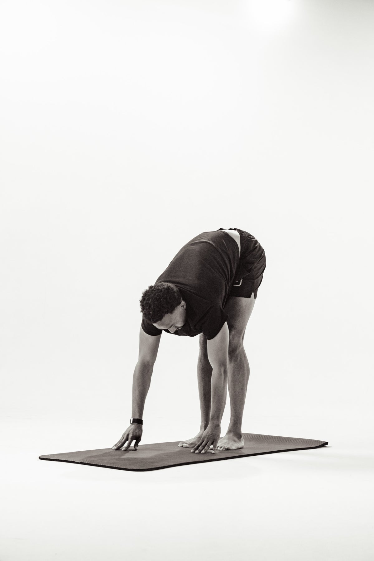 A man in a forward fold on an exercise mat in a bright studio