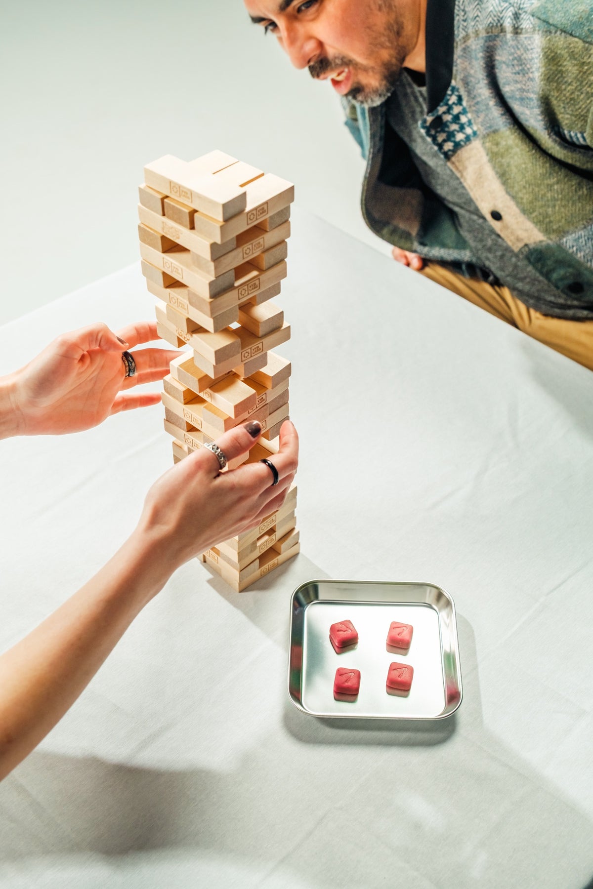 Two people playing a wooden block tower game at a table with Vybrance Labs gummies on a metal tray