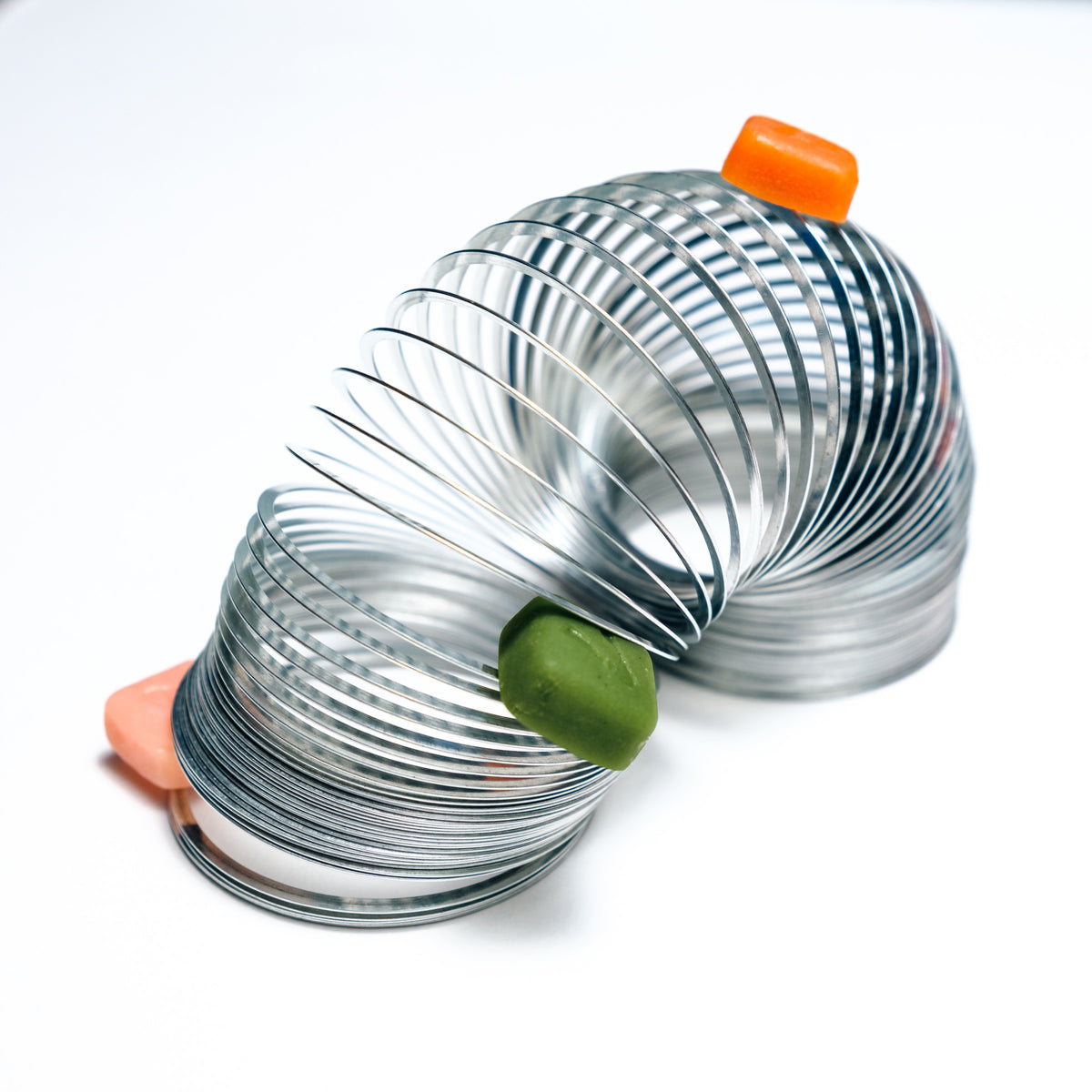 Three Vybrance Labs creatine gummies resting in the coils of a metal slinky on a white surface