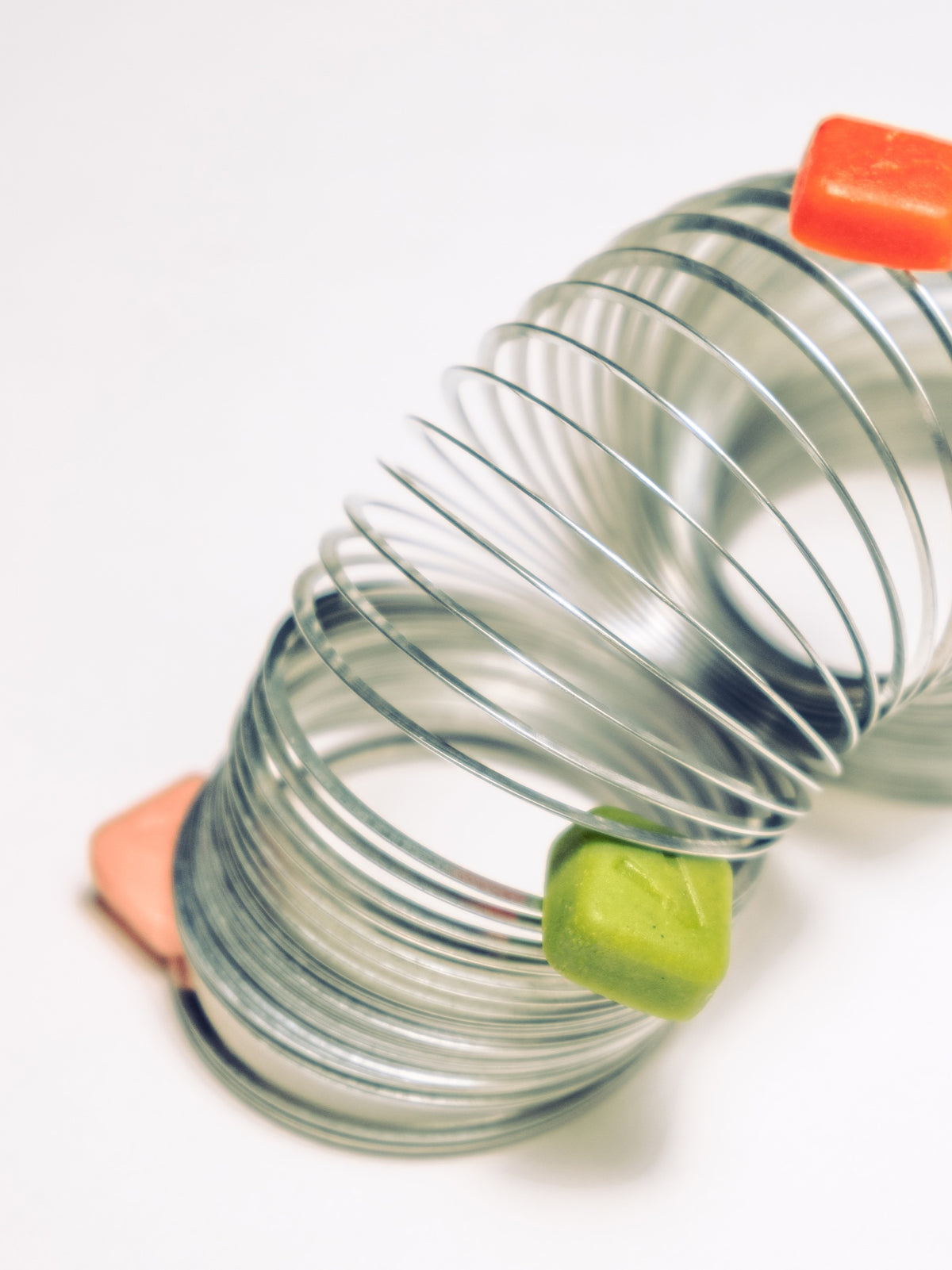 A metal spring toy stretched across a white tabletop with an orange and a green gummy resting on its coils
