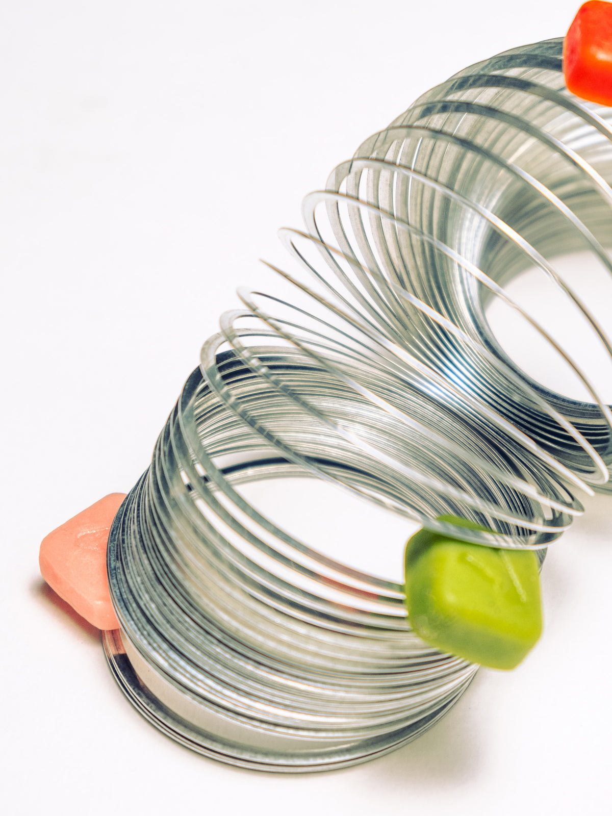 A long metal coil spring stretched across a white background with creatine gummies at both ends