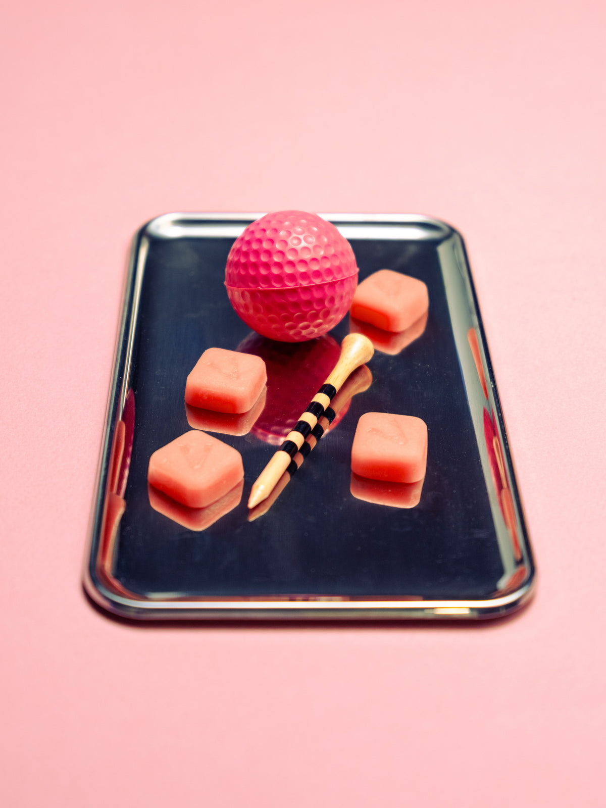 Creatine gummies and a pink ball laid out in neat rows on a dark tray against pink