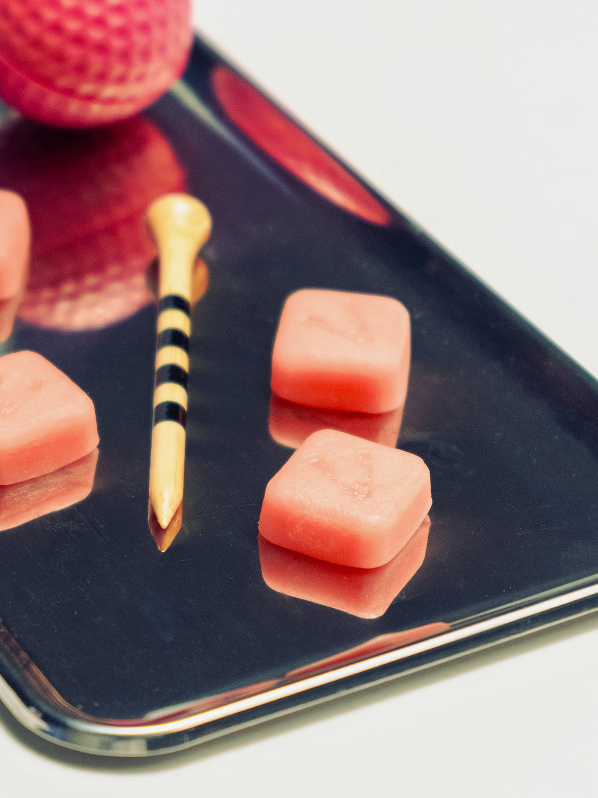 Creatine gummies arranged on a dark metal tray beside a striped wooden tee