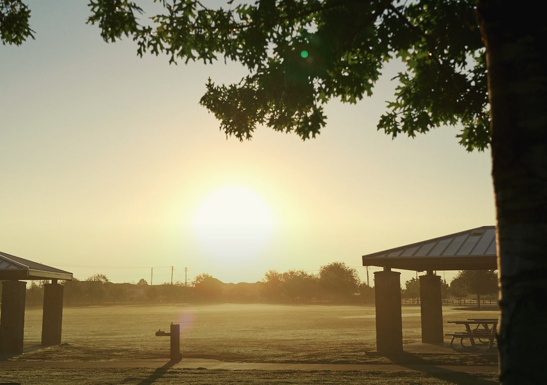 Sunrise over a park pavilion and empty picnic table in Austin, early morning light across the field.