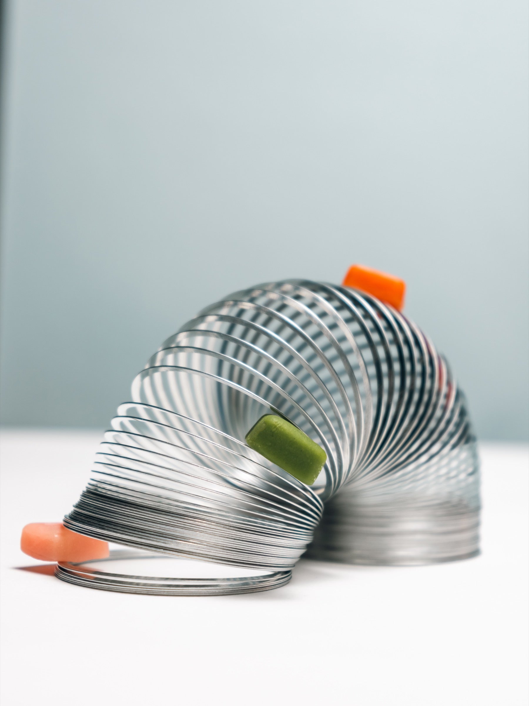 Three Vybrance Labs creatine gummies — watermelon, citrus mango, and green apple — riding the coils of a steel slinky in motion