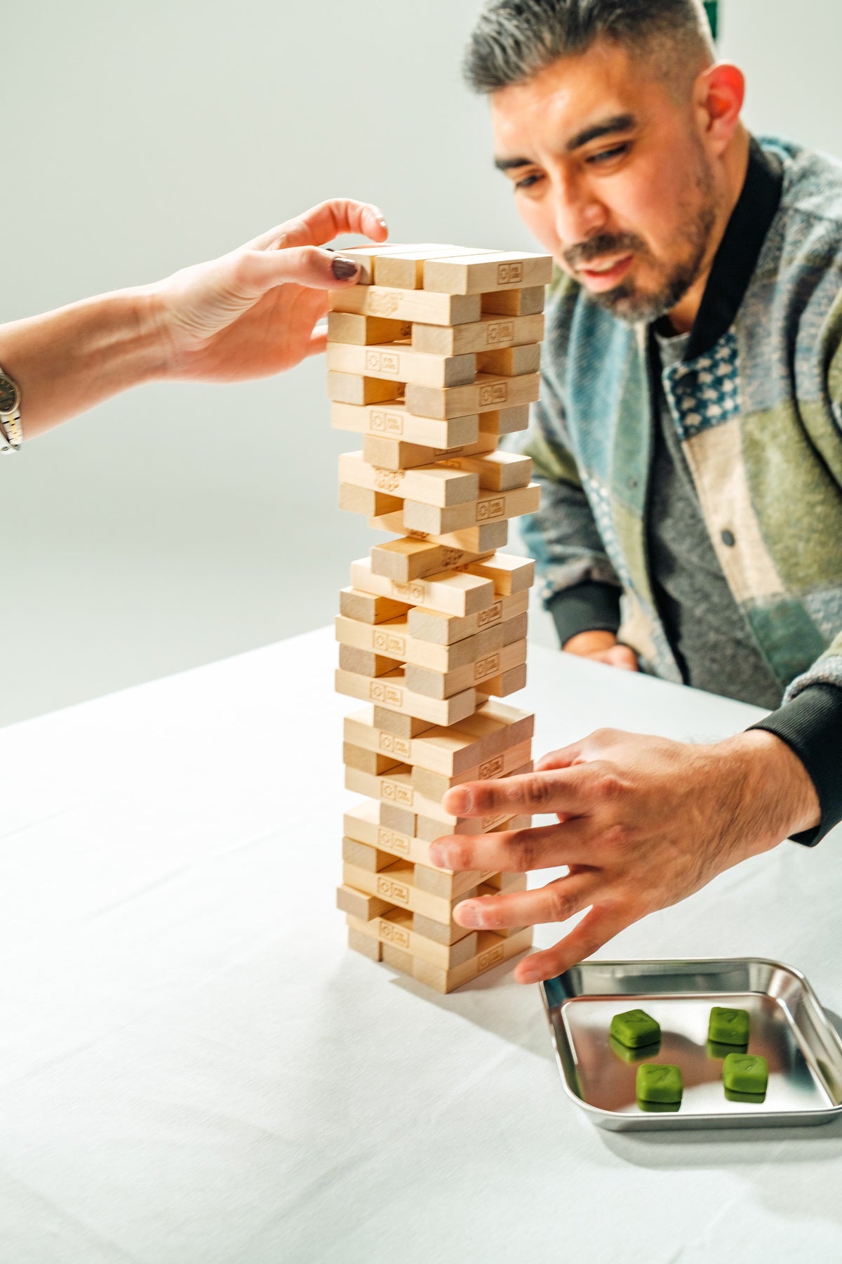 A man concentrating as he steadies a tall tower of wooden blocks on a white table